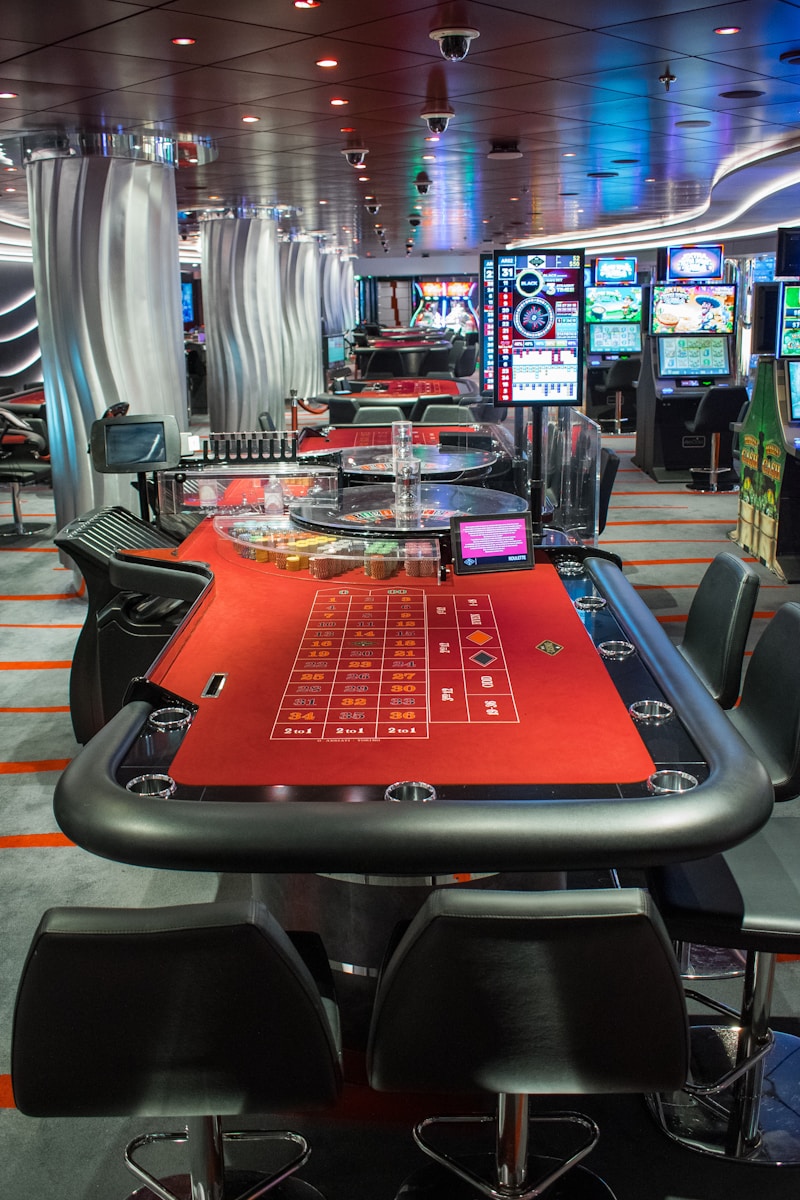 a casino room with a red table and black chairs